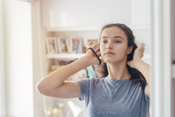 young girl straightens her hair while holding hair in her hands, reflected in the mirror
