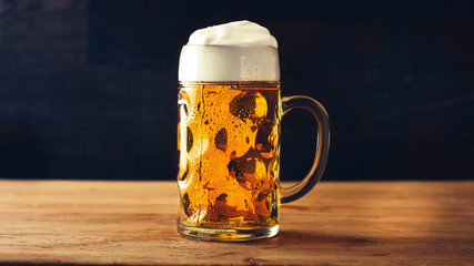Mug of fresh beer with foam on wooden table