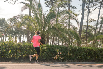 young woman with headphones makes a morning jog on the road along the pines and palm trees