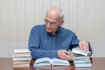 old man with glasses examines piles of books on the table