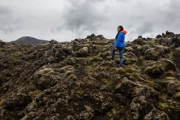 A woman stands on a moss overgrown lava field