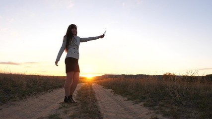 Fototapeta na wymiar beautiful business woman travels and takes a selfie photo using mobile smartphone on the road against the sunset. concept of tourism. Girl tourist in the field makes selfie with tablet