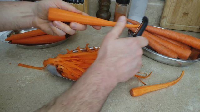 Home cooking - Making thin long slices of carrots by using peeler cutting vegetable along long way and slowly spin to continue creating more stripes.