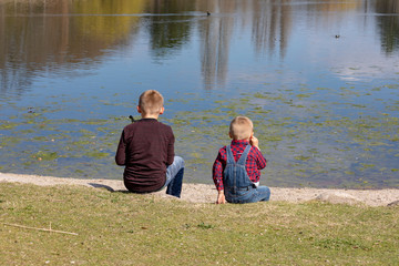 Fototapeta premium Children sit together at the lake and look out to the water