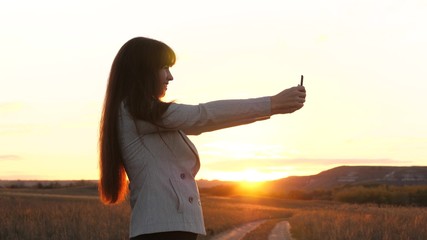 Girl tourist in the field makes selfie with tablet. beautiful business woman travels and takes a selfie photo using mobile smartphone against the backdrop of the sunset. concept of tourism