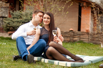 Young couple in love sitting on a picnic blanket in a park, drinking wine and enjoy each other