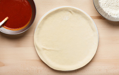 Pizza preparation. Raw pizza base and sauce in bowl