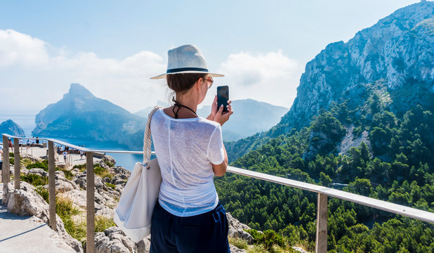 Back view of a woman taking photograph with a smart phone camera. Pretty female  tourist is taking pictures of the Mountain.