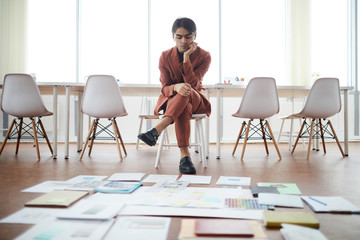 Full length portrait of contemporary Middle-Eastern businessman planning creative project in office with papers laying on floor, copy space