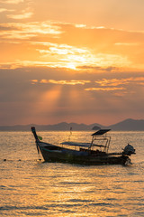 Golden sun rays and local empty thai long-tail boat under them in sea water at beautiful orange sunset