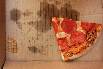 Last pepperoni pizza slice in delivery box top view. Single leftover slice of original fresh pepperoni pizza, classic italian cuisine, in paper box from take out