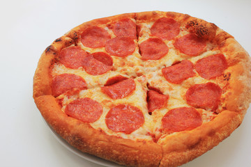 Pepperoni pizza served on plate isolated on empty white table background. Traditional italian style pizza made with natural organic pepperoni sausage, mozzarella cheese and tomato sauce