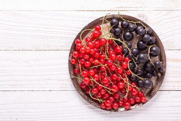 Fresh red and black currant on the vintage metal plate on a white wooden background Top view