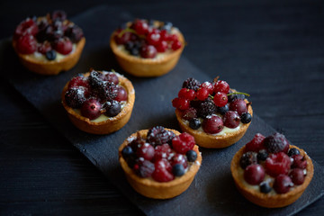 Sweet tarts with vanilla custard and berries on black wooden background