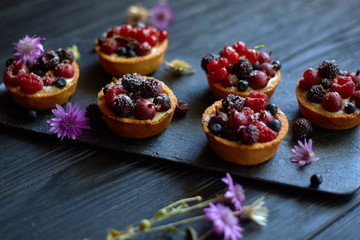 Sweet tarts with vanilla custard and berries on black wooden background