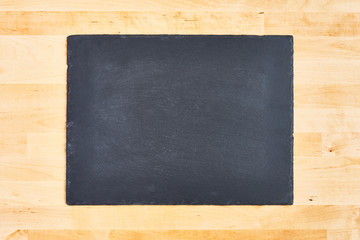 Black slate or black stone serving plate over wooden background. Copy space for text or design.
