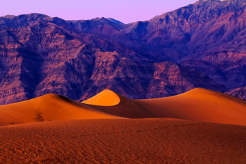 Fototapeta na wymiar Vivid colors of sunset in Death Valley National Park with purple mountains behind sand dunes.