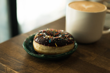coffee with a heart made of milk and a donut on a wooden table. Bad breakfast