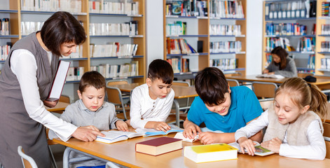 Fototapeta na wymiar Group of school kids studying in school library with friendly female teacher