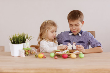 A girl with an older brother are sitting at the holiday table and laying out cookies and Easter eggs
