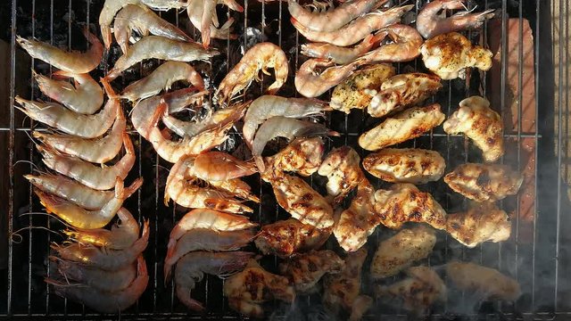 Manos dando vuelta a las gambas y piezas de pollo en barbacoa al aire libre