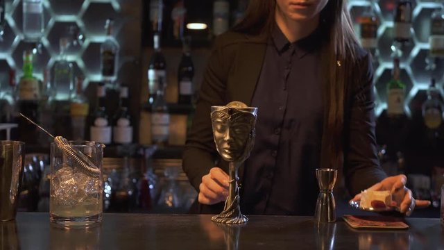 Woman put on top of bowl metal sauser with pieces of cheese, dry roses and raspberry. Metal cup with beverage on the bar.