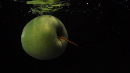 Slow motion shot: green apple falls and floats in water. Black background. Food video apple - Powered by Adobe