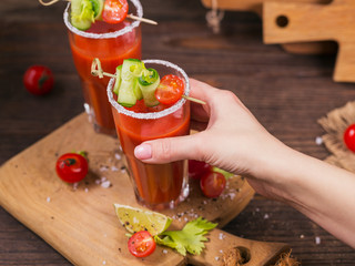 Two glasses of tomato juice decorated with fresh tomatoes, cucumber and leaves on a wooden background