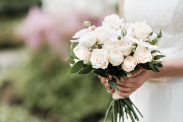 Bridal bouquet with pink and cream roses in the hands of the bride.