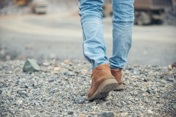 Travel and success concept. Picture of feet of person back view (lonely girl), wearing brown leather boots and blue jeans. Foot of traveler Walk toward successful on path way.
