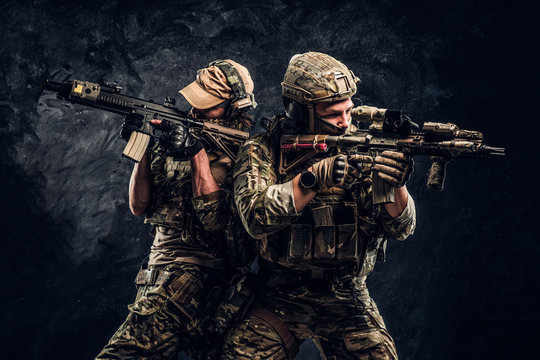 Private security service contractors, the elite special unit, full protective soldiers aiming at the targets. Studio photo against a dark wall.