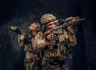 Two special forces soldiers in full protective equipment holding assault rifles and aiming at the...