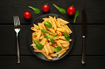Penne pasta in tomato sauce and decorated with greens on a wooden background, top view