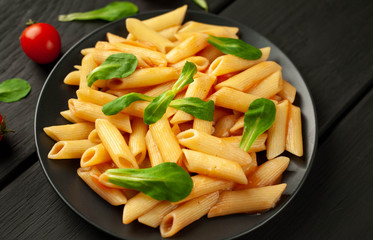 Penne pasta in tomato sauce and decorated with greens on a wooden background, top view