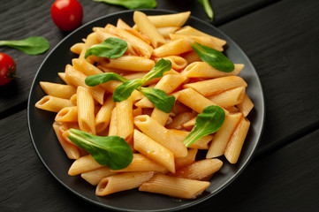 Penne pasta in tomato sauce and decorated with greens on a wooden background, top view