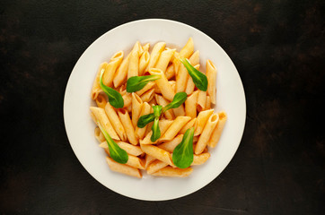 Penne pasta in tomato sauce and decorated with greens on a background of concrete, top view