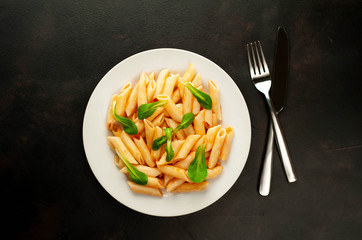 Penne pasta in tomato sauce and decorated with greens on a background of concrete, top view