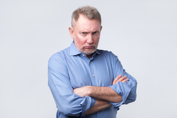 Senior man holding hands crossed on chest, looking from under forehea