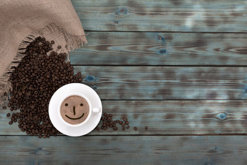 Roasted brown coffee grains and a cup of coffee lie on blue wooden boards.