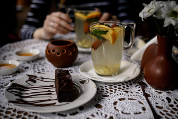 hands of the girl hold a transparent cup of tea with cinnamon, mint, orange on the table with a beautiful decor and dessert . warming fruit mint tea in the restaurant