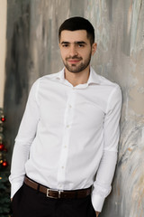 Fototapeta na wymiar Male portrait. Handsome brunette man in white shirt and classy black jeans poses in grey studio