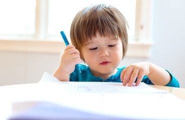 Toddler boy drawing with pen and paper at his desk