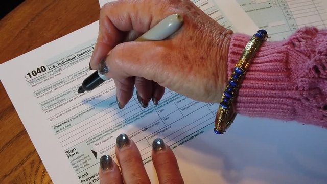 Woman's hands writing Scam Alert on a federal tax form with a marker. The hands are Caucasian. She has long nails nail polish.