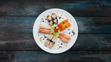 Rotating sashimi set on a white round plate, decorated with small flowers, Japanese food, top view. Wooden background with the copy space for your text