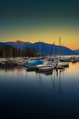 Obraz premium Dark green and yellow sunset with boats in the port of Ascona, Switzerland