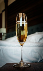 A glass of champagne, luxury bedroom interior on the background. Expensive hotel stay concept.