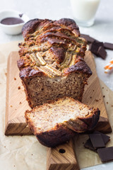 Banana bread or loaf cake with chocolate on a wooden cutting board. Copy space.