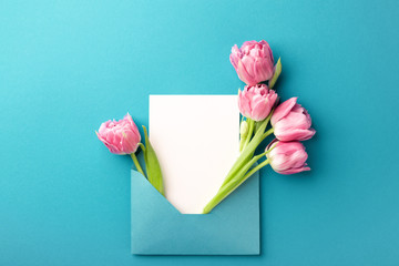 Bouquet of pink tulips in turquoise envelope on turquoise background. Mockup with white card. Flat lay, top view.