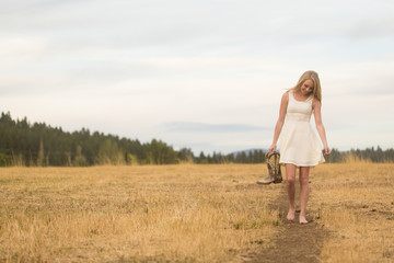 Naklejka na ściany i meble Beautiful young lady walking barefoot on path in country field