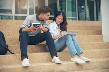 Study and technology concept.Asian Student reading book studying for an exam and using mobile phone at university.Happy woman and man successfully completes the thesis report and passed the final exam